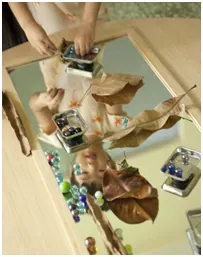 Children exploring leaves and glass beads on a mirror
