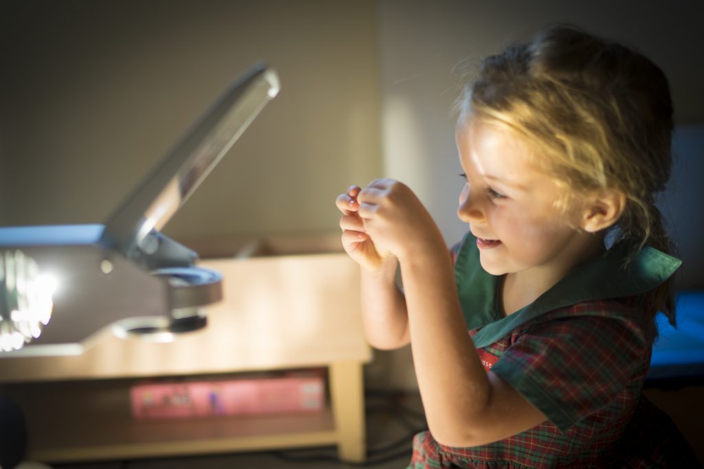 Young child examining a small object under a lamp in the classroom