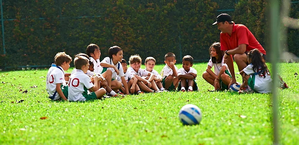 Primary students sitting on a football pitch with their coach