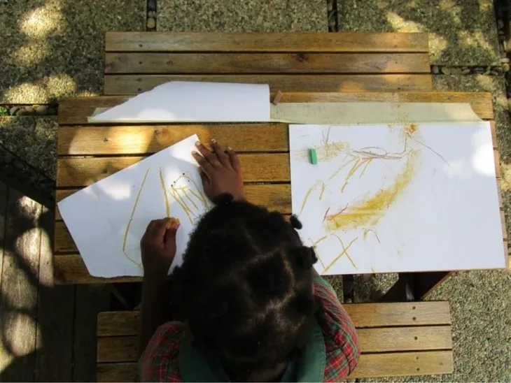 Child drawing with crayons at an outdoor table